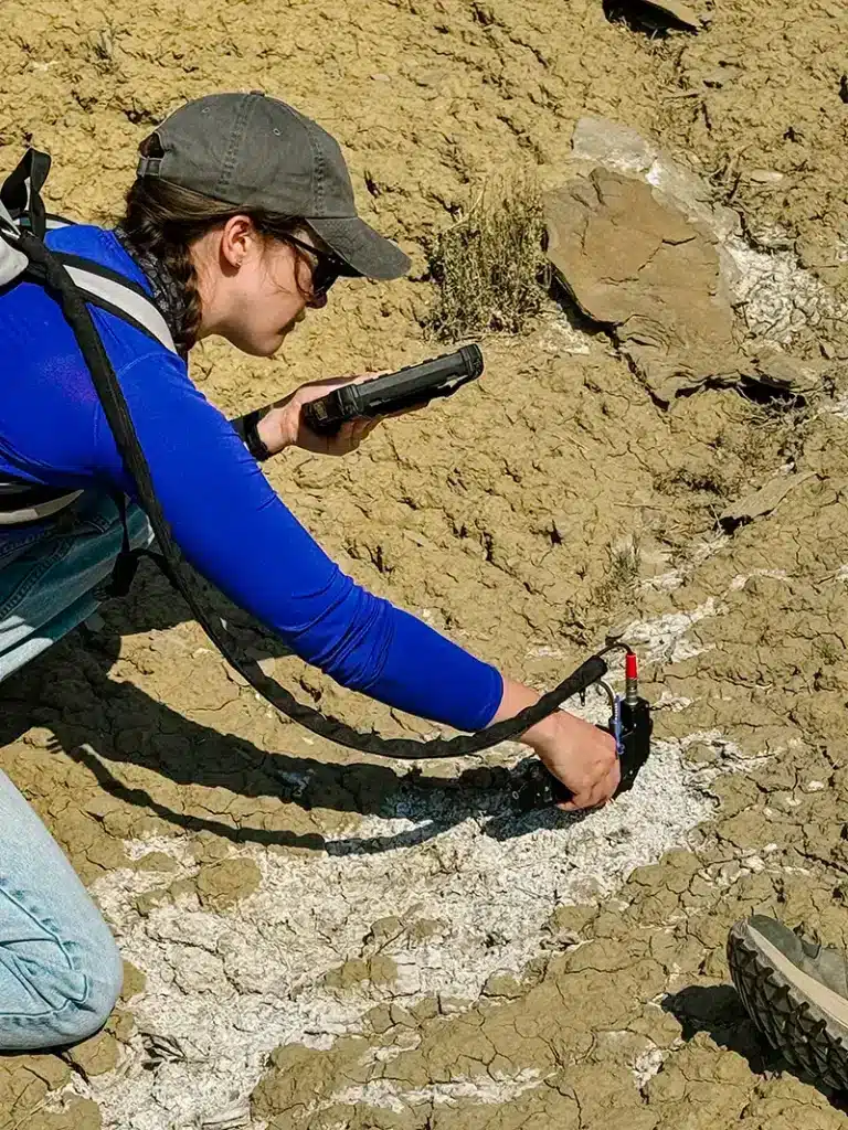 Sarah Shield works in the field with tools to analyze rocky ground and soil.